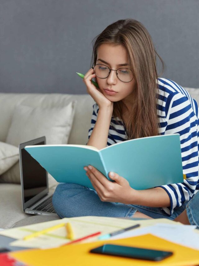 a young girl is sitting on sofa and studying for exams